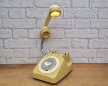 Load image into Gallery viewer, A quirky lamp made from a retro phone. The base of the lamp is a classic mustard rotary phone with a cream-colored dial ring. The cream handset mounted on a flexible gooseneck has a small LED bulb in the receiver converting it into a fabulous lamp.