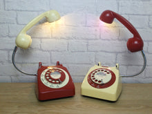 Load image into Gallery viewer, A pair of lamps made from retro phones. The bases of the lamps are rotary phones, one red one cream with alternating colours for the dials & the handsets  which are on a flexible gooseneck with small LED bulbs in the receiver converting them to lamps