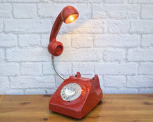 Load image into Gallery viewer, A quirky lamp made from a retro phone. The base of the lamp is a classic red rotary phone with a clear dial ring. The red handset mounted on a flexible gooseneck has a small LED bulb in the receiver converting it into a fabulous lamp.