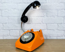 Load image into Gallery viewer, A quirky lamp made from a retro phone. The base of the lamp is a bright orange rotary phone with a black colored dial ring. The black handset mounted on a flexible gooseneck has a small LED bulb in the receiver converting it into a fabulous lamp.