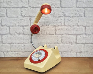 A quirky lamp made from a retro phone. The base of the lamp is a cream rotary phone with a red ring & alpha numeric dial. The cream handset mounted on a flexible gooseneck has a small LED bulb in the receiver converting it into a fabulous lamp.