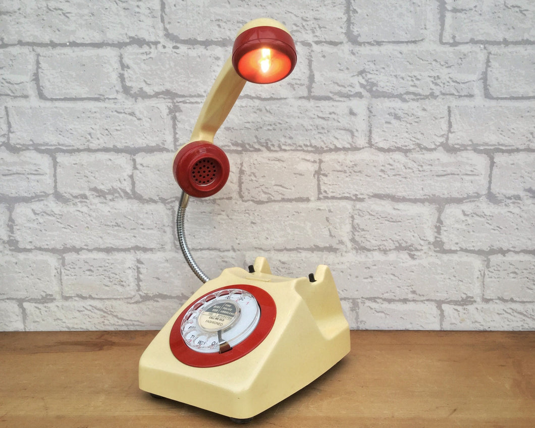 A quirky lamp made from a retro phone. The base of the lamp is a cream rotary phone with a red ring & alpha numeric dial. The cream handset mounted on a flexible gooseneck has a small LED bulb in the receiver converting it into a fabulous lamp.