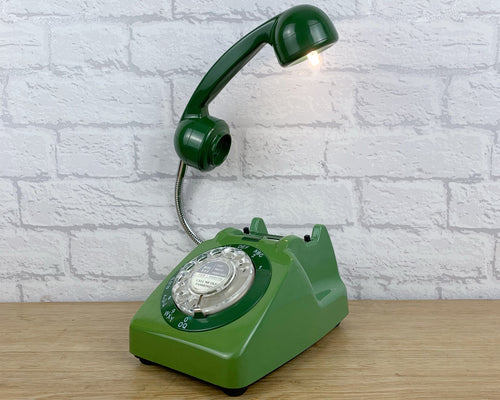 A quirky lamp made from a retro phone. The base of the lamp is a classic green rotary phone with a darker green dial ring. The dark green handset mounted on a flexible gooseneck has a small LED bulb in the receiver converting it into a fabulous lamp.
