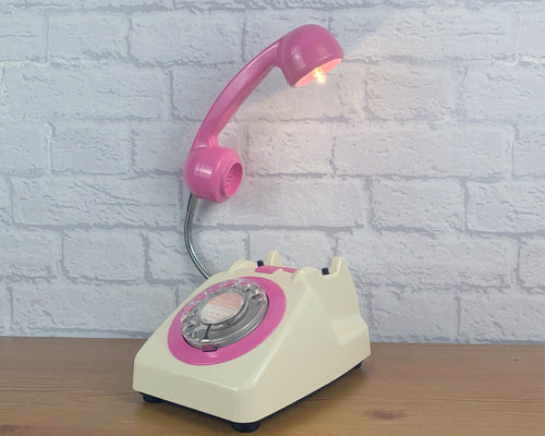 A quirky lamp made from a retro phone. The base of the lamp is a classic cream rotary phone with a hot pink dial ring. The hot pink handset mounted on a flexible chrome gooseneck has a small LED bulb in the receiver converting it into a unique lamp.